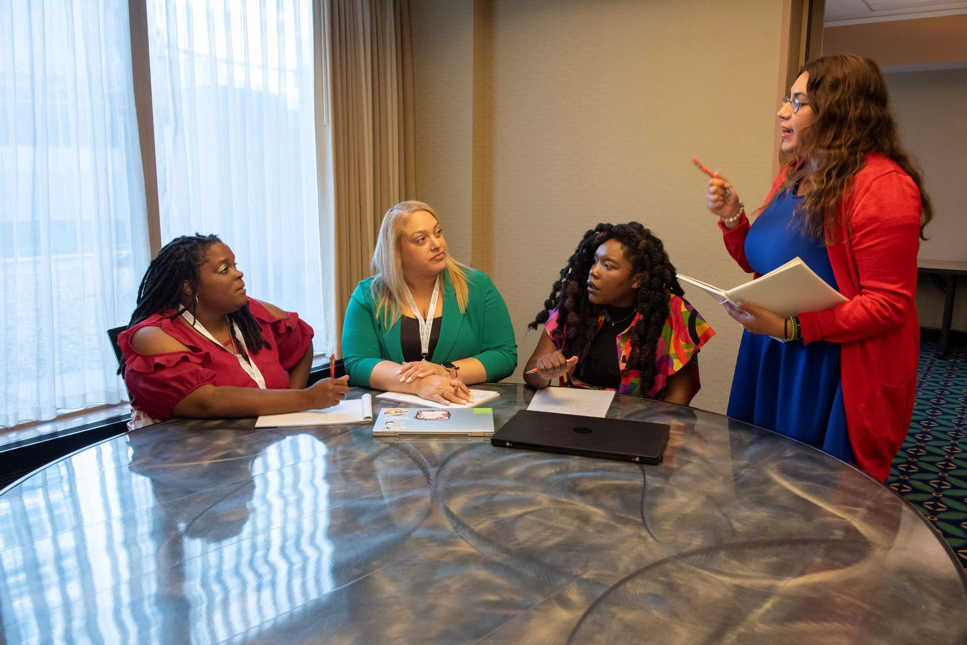 Facilitator leading a peer-to-peer support group discussion among women seated around a table.
