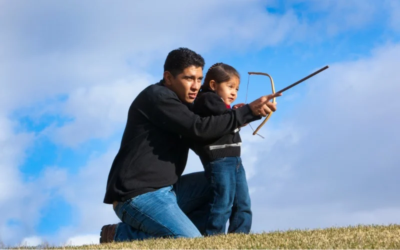 A father and a daughter playing outdoor with a bow